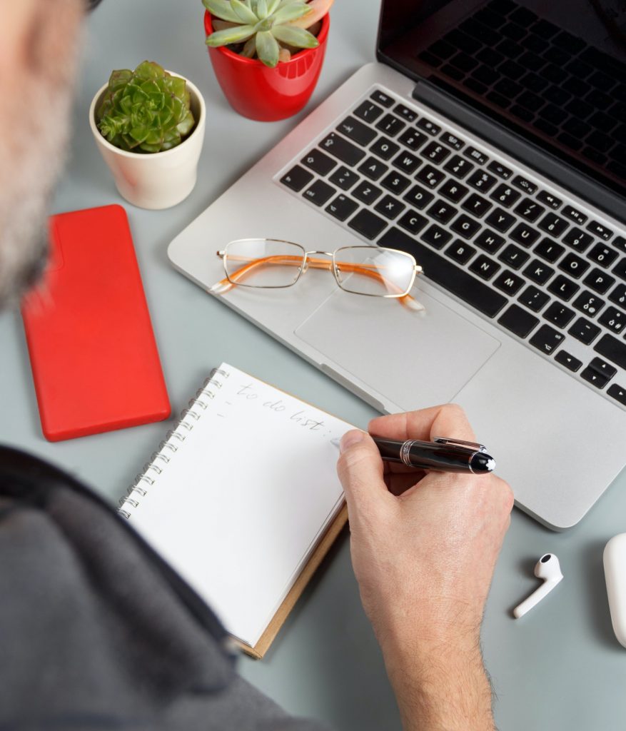 Man writing TO DO LIST near laptop on a grey office desk close up